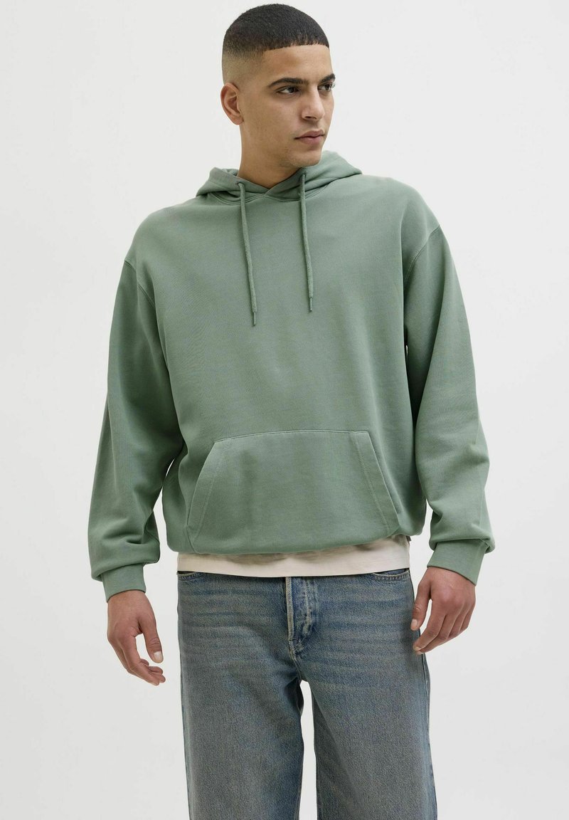 Light green hoodie with a front pocket, drawstrings, and ribbed cuffs paired with blue jeans. Soft texture, casual design.