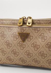 Braune Handtasche mit Muster und goldenen Beschlägen, ausgestattet mit einem doppelten Reißverschluss und einem dreieckigen Logo-Detail auf der Vorderseite.