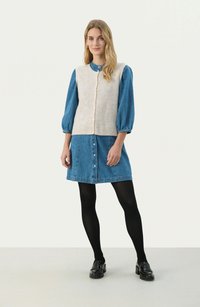 Beige knitted vest with button closure over a blue denim shirt dress. Styled with opaque black tights and black loafers.
