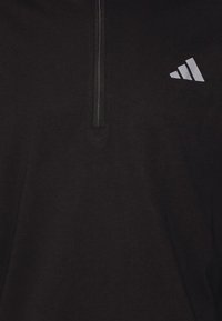 Veste noire à fermeture éclair quart de zip avec une fermeture verticale et un logo Adidas blanc sur la partie supérieure gauche de la poitrine.