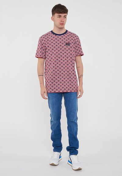 T-shirt a maniche corte rosso e bianco a fantasia con colletto blu navy, abbinato a jeans blu dritti e sneakers bianche.