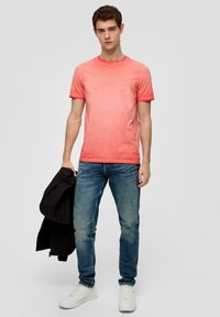 Camiseta de manga corta en degradado rojo con cuello redondo, combinada con jeans de denim azul y zapatillas blancas, junto con una chaqueta negra.