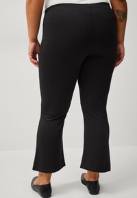 Leggings flare neri in cotone misto con una texture liscia, vita media e orlo che finisce appena sopra la caviglia.