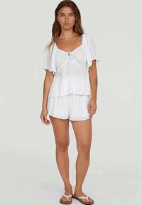 White two-piece outfit featuring a flowy top with a tie front and short sleeves, paired with matching shorts. Light, airy fabric.