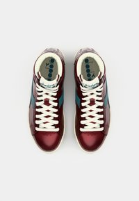 High-top sneakers featuring glossy maroon and teal panels, white laces, and beige soles. Interior has printed logo on light fabric.