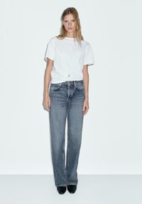 T-shirt bianco in cotone con maniche corte, abbinato a jeans grigi scuri a gamba dritta a vita alta. Tacchi neri completano il look.
