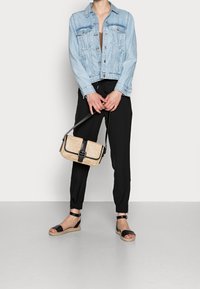Chaqueta de mezclilla azul claro, pantalones jogger negros, bolso cruzado de tejido marrón con acentos negros, y sandalias negras con correas en los tobillos.