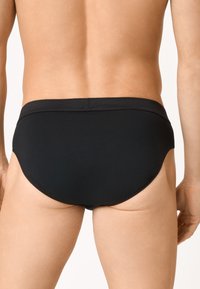 Slips de bain pour hommes noirs avec un tissu lisse et extensible, taille basse et design à couverture minimale, arborant un dos propre et simple.