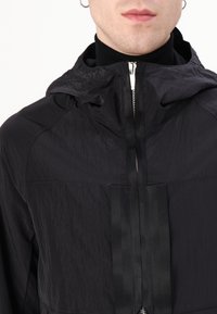 Black hooded jacket made from lightweight, textured fabric. Features a central zip with a sleek panel design and contrasting satin details.