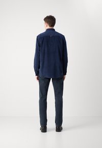 Camicia in velluto a coste blu marina con maniche lunghe, colletto button-down e una piccola etichetta con logo sulla parte superiore della schiena. Abbinata a jeans in denim scuro e scarpe nere.