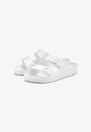 Weiße Sandalen mit zwei verstellbaren Riemen, die ein strukturiertes Obermaterial und eine glatte Gummisohle aufweisen. Minimalistisches Design und sichere Schnallen.