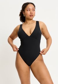 Maillot de bain une pièce noir avec un décolleté en V profond, des bretelles larges et des jambes échancrées, fabriqué en matériau lisse et extensible.