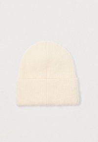 Cremfarvet ribbet strikhue med foldet kant, vist fladt mod en neutral hvid baggrund.