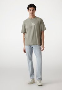 Lys grøn oversized t-shirt med rund hals og "Guess Los Angeles" trykt i hvid. Båret sammen med lyseblå jeans og hvide sneakers.