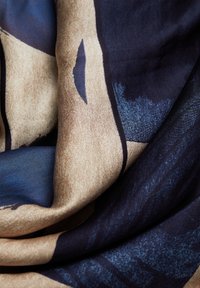 Silk scarf featuring abstract patterns in dark blue and beige. Soft texture with flowing drape, highlighting contrasting shades and shapes.