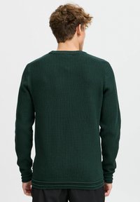 Pull vert foncé avec un design en tricot texturé de type gaufre. Manches longues et col rond. Détails côtelés subtils à l'ourlet et aux poignets.
