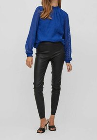 Blue patterned long-sleeve blouse with a gathered neckline, paired with tight-fitting black leather pants and black open-toe heels.