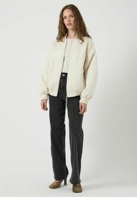 Giacca bomber trapuntata color crema con motivo testurizzato, polsini e colletto a coste. Abbinata a jeans neri a vita alta e tacchi color taupe.