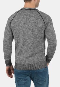 Pull en tricot gris avec des poignets et un ourlet côtelés, présentant un motif texturé. Le dos montre un design de manches raglan et un col rond.