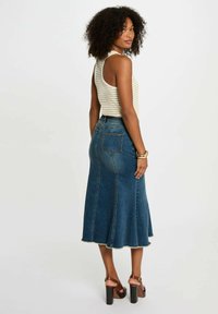 Gonna di jeans a trapezio con orlo sfrangiato, di colore blu intenso, e due tasche posteriori. Abbinata a un top senza maniche a righe e sandali con platform marroni.