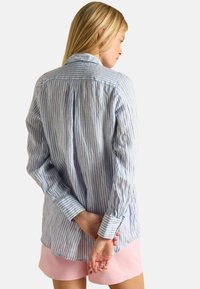 Heledad sinise ja valge triibuga pikkade varrukatega särk, mis on valmistatud puuvillast. Särgil on tagaküljel volditud disain ja nööbid mansettidel. Sobitatud roosa lühikeste pükstega.