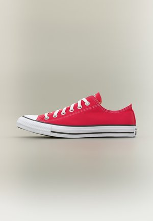 Czerwony niski tenis z materiału z białym gumowym noskiem, białymi sznurowadłami i podeszwą w czarne paski na jednolitym jasnym tle.