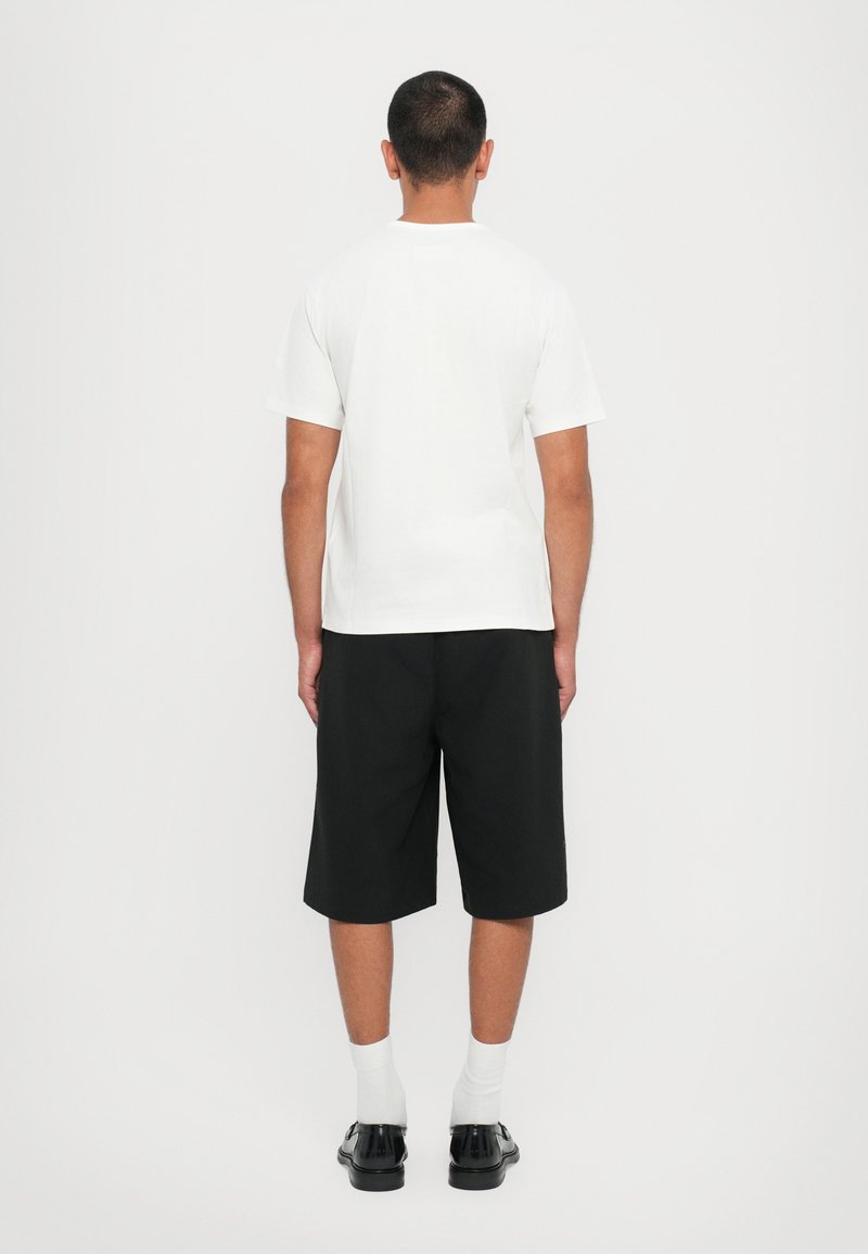 T-shirt bianco a maniche corte con scollo rotondo, abbinato a pantaloni corti neri fino al ginocchio. Indossato con calze bianche e scarpe nere.