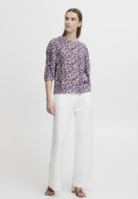 Floral blouse with 3/4 sleeves in purple, pink, and blue on a white background; paired with wide-legged white pants and neutral sandals.