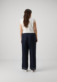 White, textured top with scalloped sleeves paired with navy, pleated wide-leg pants, featuring a relaxed fit and elastic waistband.