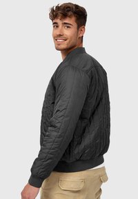 Black quilted bomber jacket with ribbed cuffs and waistband, featuring a stand collar and side pockets. Textured surface with subtle sheen.