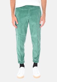 Pantaloni in velluto a coste verde con vestibilità slim, caratterizzati da una superficie a coste testurizzate e orli arrotolati. Abbinati a sneaker bianche.