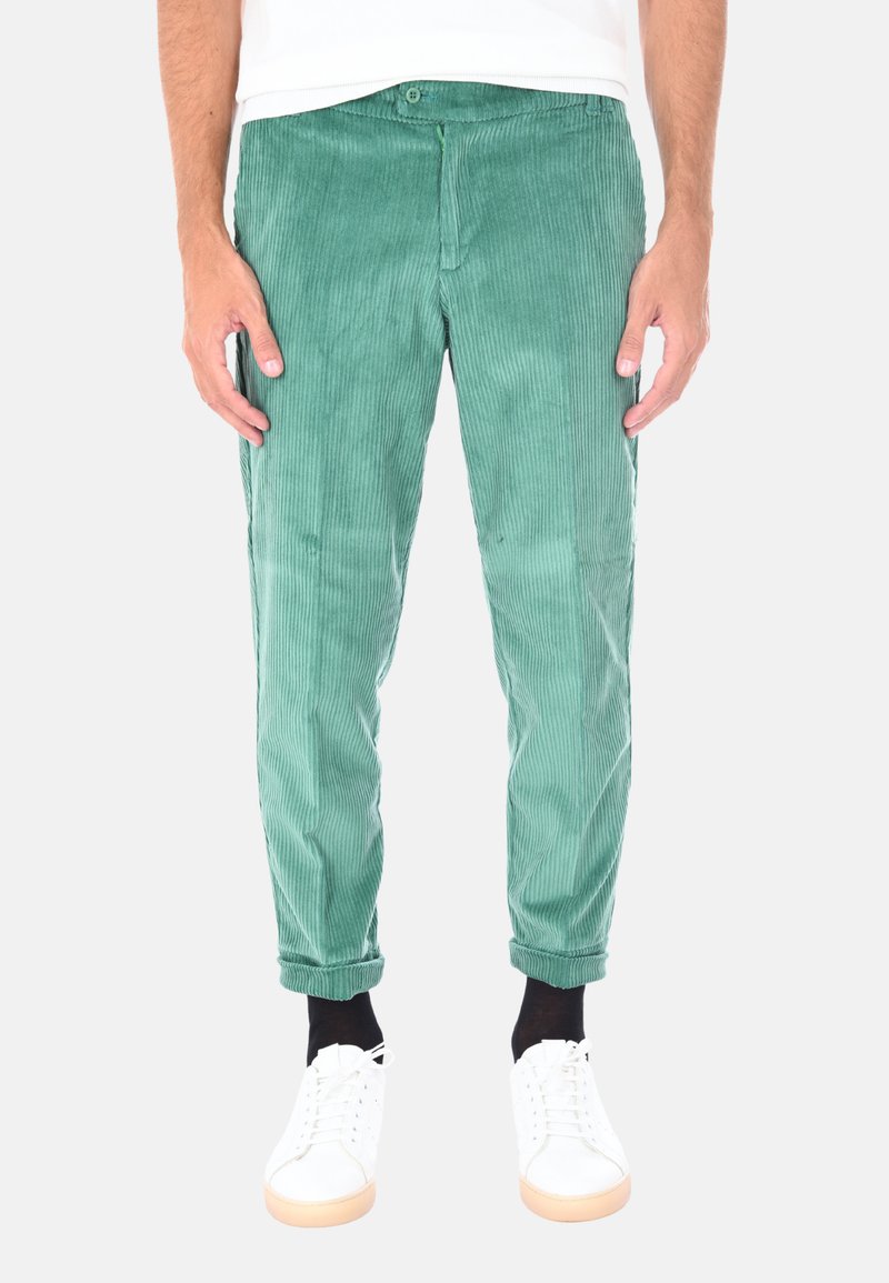 Pantaloni in velluto a coste verde con vestibilità slim, caratterizzati da una superficie a coste testurizzate e orli arrotolati. Abbinati a sneaker bianche.