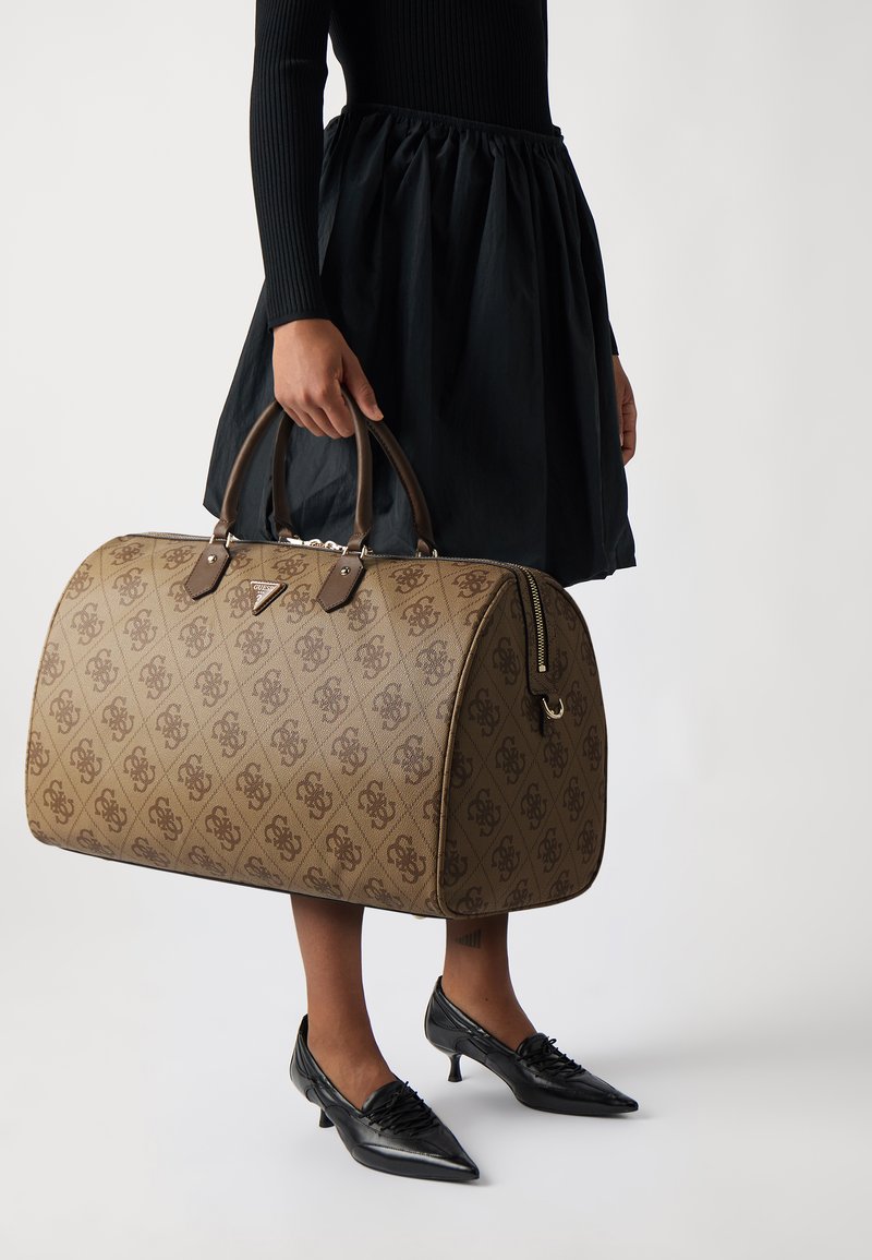 Grand sac à main marron à motifs avec des accents en cuir marron foncé et des poignées, doté d'une fermeture éclair et d'un logo sur le devant.