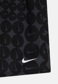 Crni sportski materijal s uzorkom tamnih krugova i malim Nike logotipima. Bijeli Nike swoosh vidljiv je duž donjeg ruba.