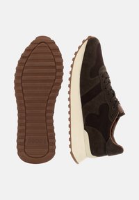 Bruna mocka sneakers med mörka accenter, texturerad brun gummisula och vit mellansula. Snörningarna är svarta och har en distinkt design.