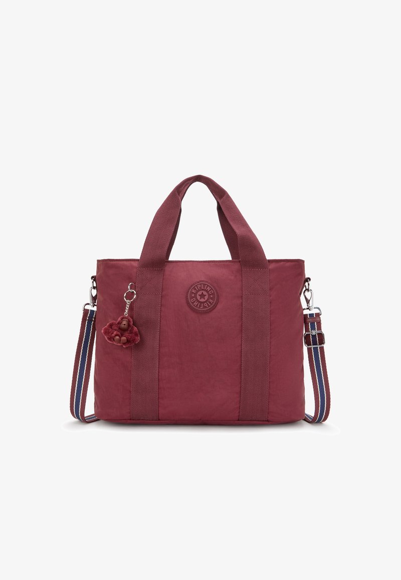 Maroon tote bag made of textured fabric with dual handles, detachable striped shoulder strap, and a plush monkey charm attached. Circular logo detail.