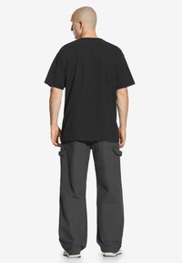 Czarna bawełniana koszulka z luźnym krojem, krótkimi rękawami i okrągłym dekoltem. Połączona z luźnymi, ciemnoszarymi spodniami cargo z bocznymi kieszeniami.