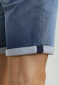 Shorts in denim con lavaggio blu scuro, con orlo arrotolato in grigio chiaro. La trama del tessuto è liscia con cuciture visibili.