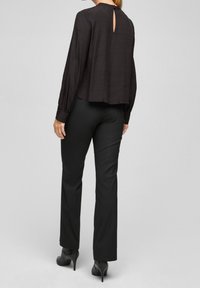 Blusa nera con texture, maniche lunghe e dettaglio a chiave sul retro, abbinata a pantaloni neri aderenti e stivali con tacco alto.