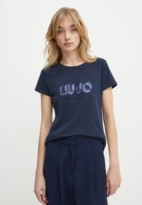 T-shirt in cotone blu navy con maniche corte caratterizzata da un logo testurizzato "LUJO Milano" in una tonalità di blu più chiara sul davanti.