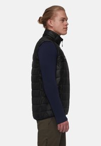 Schwarze Steppweste mit hohem Kragen, ausgestattet mit einem Reißverschluss auf der Vorderseite, seitlichen Taschen und einem gesteppten Design. Getragen über einem dunklen Langarmshirt.