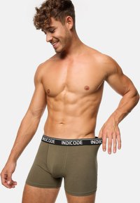 Olívazöld boxer alsónadrág fekete derékkal, amelyen fehér betűkkel az "INDICODE" felirat olvasható. Puha anyag és szűk fazon, aktív használatra alkalmas.