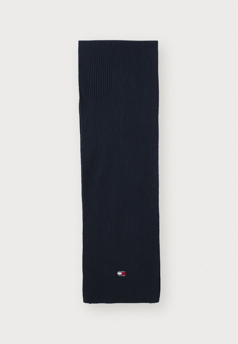 Bufanda de color navy con textura suave. Presenta un pequeño parche con el logo en la parte inferior. Forma rectangular, adecuada para el uso invernal.