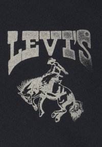 Μαύρο ύφασμα με ένα λογότυπο Levi's σε παλιό στυλ και φθορά, σε ασημί χρώμα, καθώς και μια γραφική παράσταση ενός αναβάτη σε άλογο.
