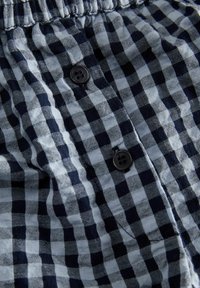 Tissu à carreaux bleu marine et bleu clair avec une texture douce, comprenant deux boutons noirs et une taille élastique. Détail d'un vêtement décontracté.