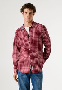 Camicia a quadri rossi e bianchi con colletto button-down, maniche lunghe e un accentuazione in denim sul colletto. Indossata con una T-shirt bianca sotto.