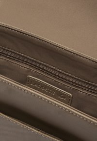 Interno della borsa a tracolla in tessuto beige con un compartimento con zip. Presenta un'etichetta in metallo e una fodera texture.