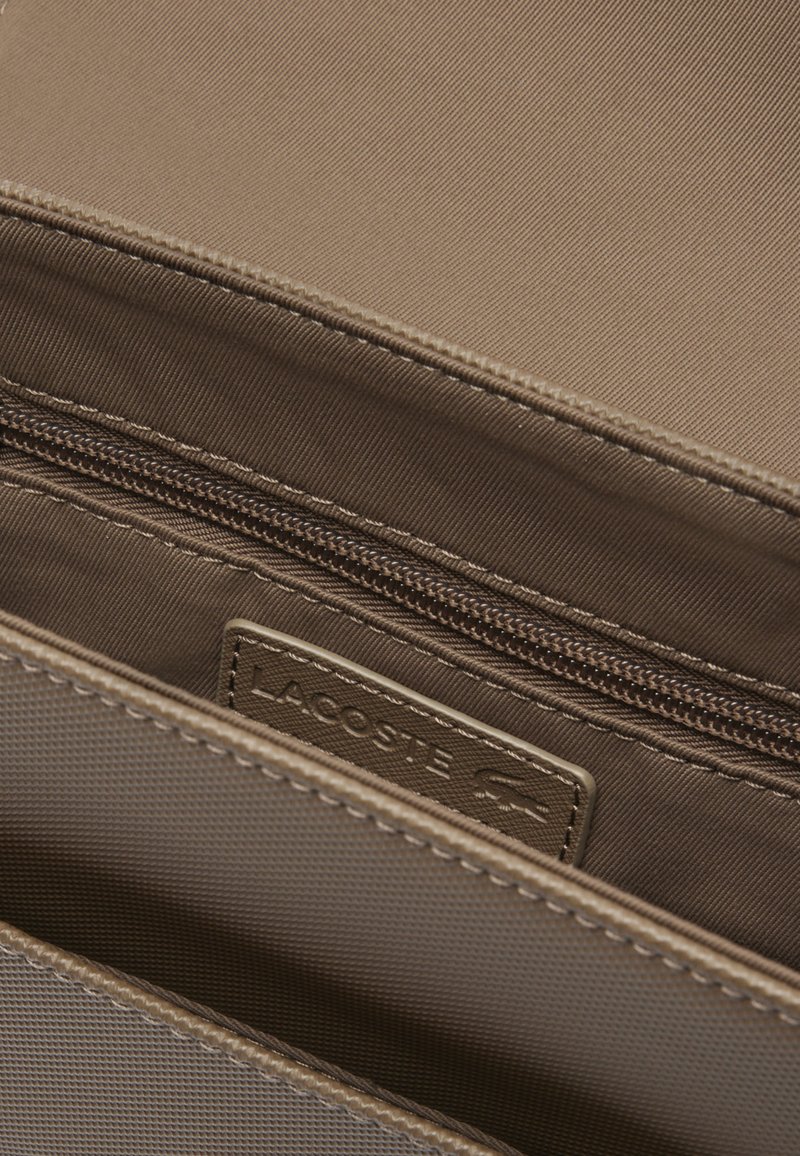 Intérieur d'un sac à main en tissu beige avec un compartiment zippé. Comprend une étiquette en métal et une doublure texturée.