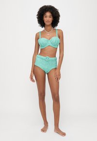 Σετ μπικίνι σε τυρκουάζ με γκλίτερ, που διαθέτει δομημένο, επενδυμένο τοπ με φαρδιές τιράντες και ψηλόμεσα σλιπ που τονίζονται από μια ζώνη.