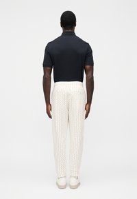 Męski strój składający się z ciemnogranatowej koszulki polo oraz kremowych spodni w geometryczne wzory, dopełniony białymi trampkami.